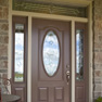 exterior view of a brown single entrance door with an oval glass panel in the centre and sidelites and transom featuring decorative glass