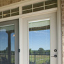 exterior patio view of beige vinyl terrace door with grey and beige fixed doors with transom featuring grills