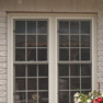 exterior patio view of twin cream stained vinyl slider windows featuring grills